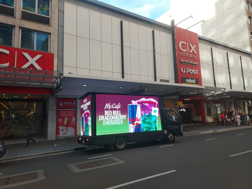 A digital billboard truck parked outside City Cross Arcade displaying a McCafé ad